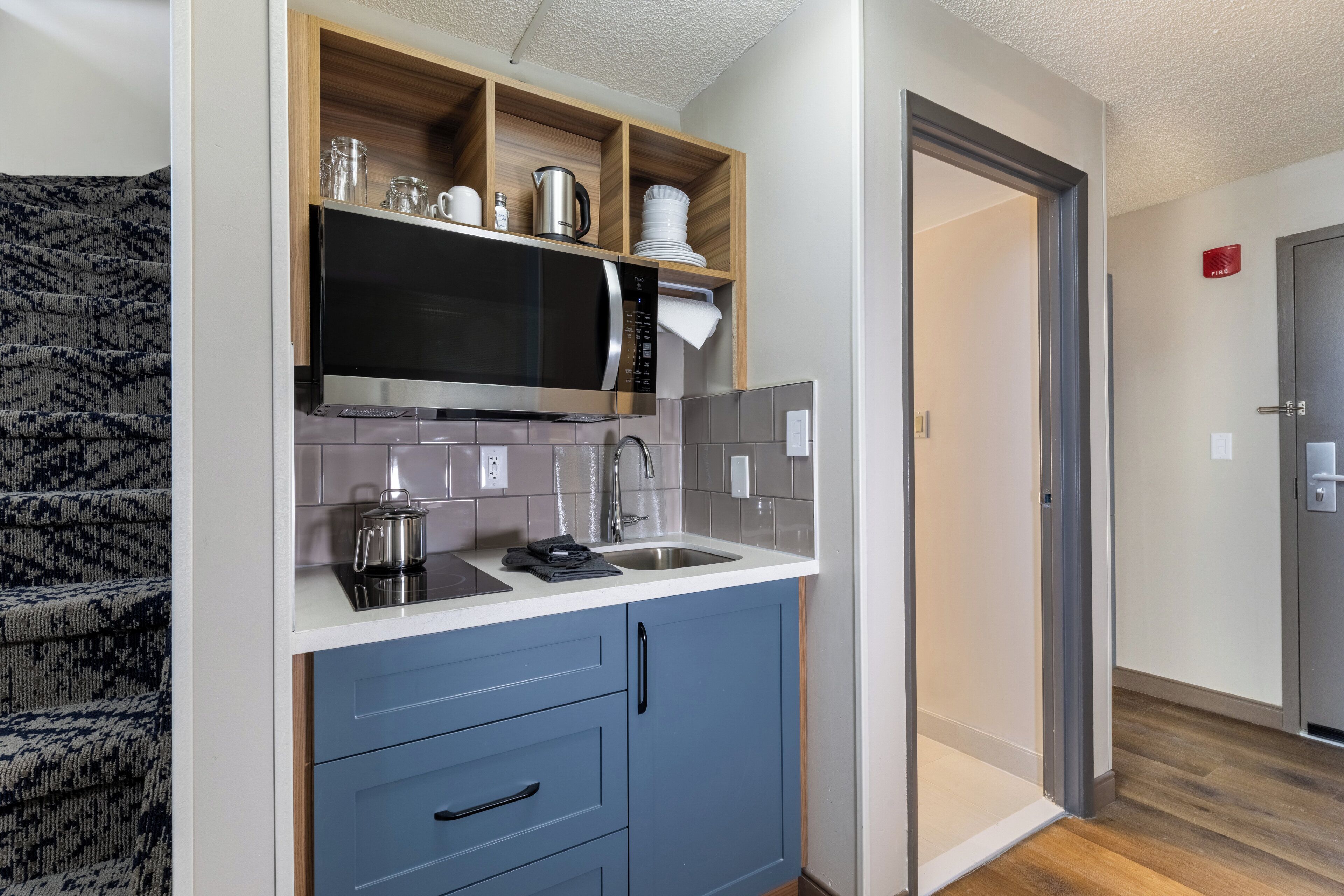 A compact kitchen with a microwave, sink, and blue cabinets.