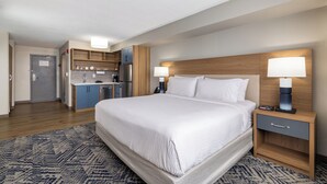A hotel room with a large bed, bedside tables, a nightstand, a desk, and a kitchenette. - Candlewood Suites London South by IHG (London)