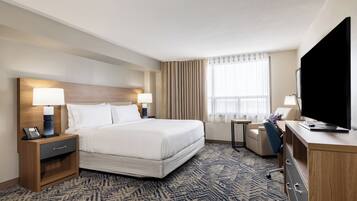 A hotel room with a large bed, bedside tables with lamps, a desk with a chair, a television, and a window with curtains.
