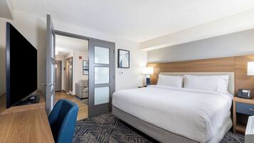 A hotel room with a large bed, a desk with a flat-screen TV, a chair, and a door leading to a bathroom.