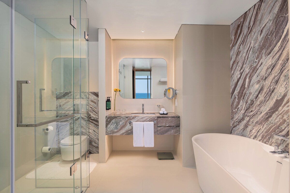 Ein modernes Badezimmer mit Duschkabine aus Glas, Marmorwaschtisch, freistehender Badewanne und großem Spiegel.