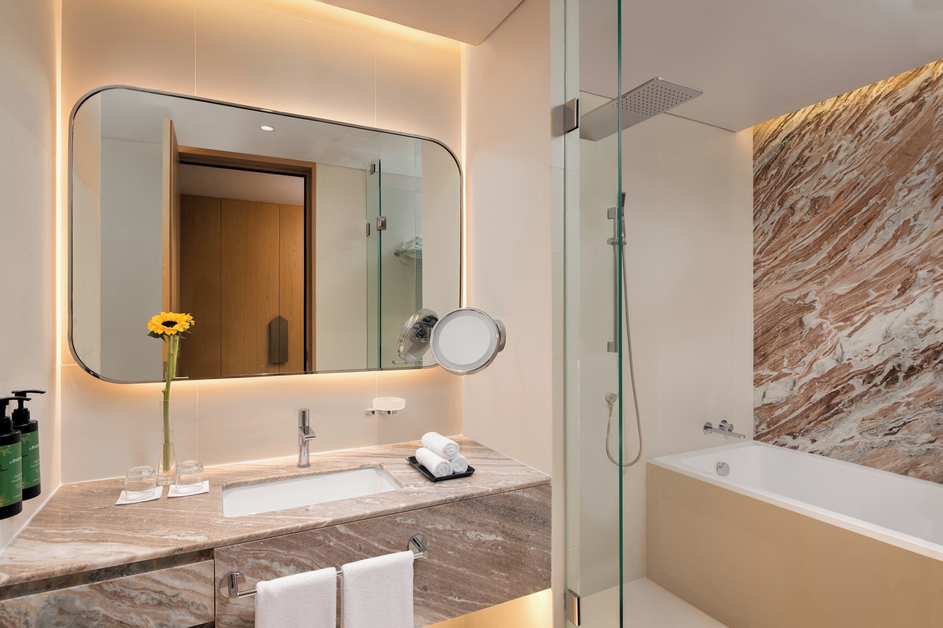 A modern bathroom with a large mirror, a sink, a glass shower enclosure, and a marble wall.