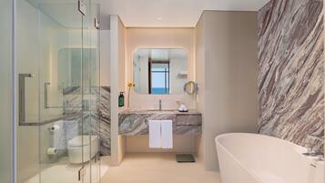 A modern bathroom with a glass shower enclosure, a marble vanity, a freestanding bathtub, and a large mirror.