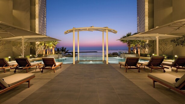 A poolside area with lounge chairs and a view of the ocean at dusk. - voco Muscat Al Mouj by IHG (Muscat)
