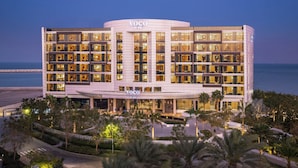 A multi-story hotel with a prominent 'Voco' sign, featuring a modern architectural design with large windows and a beachfront view. - voco Muscat Al Mouj by IHG (Muscat)