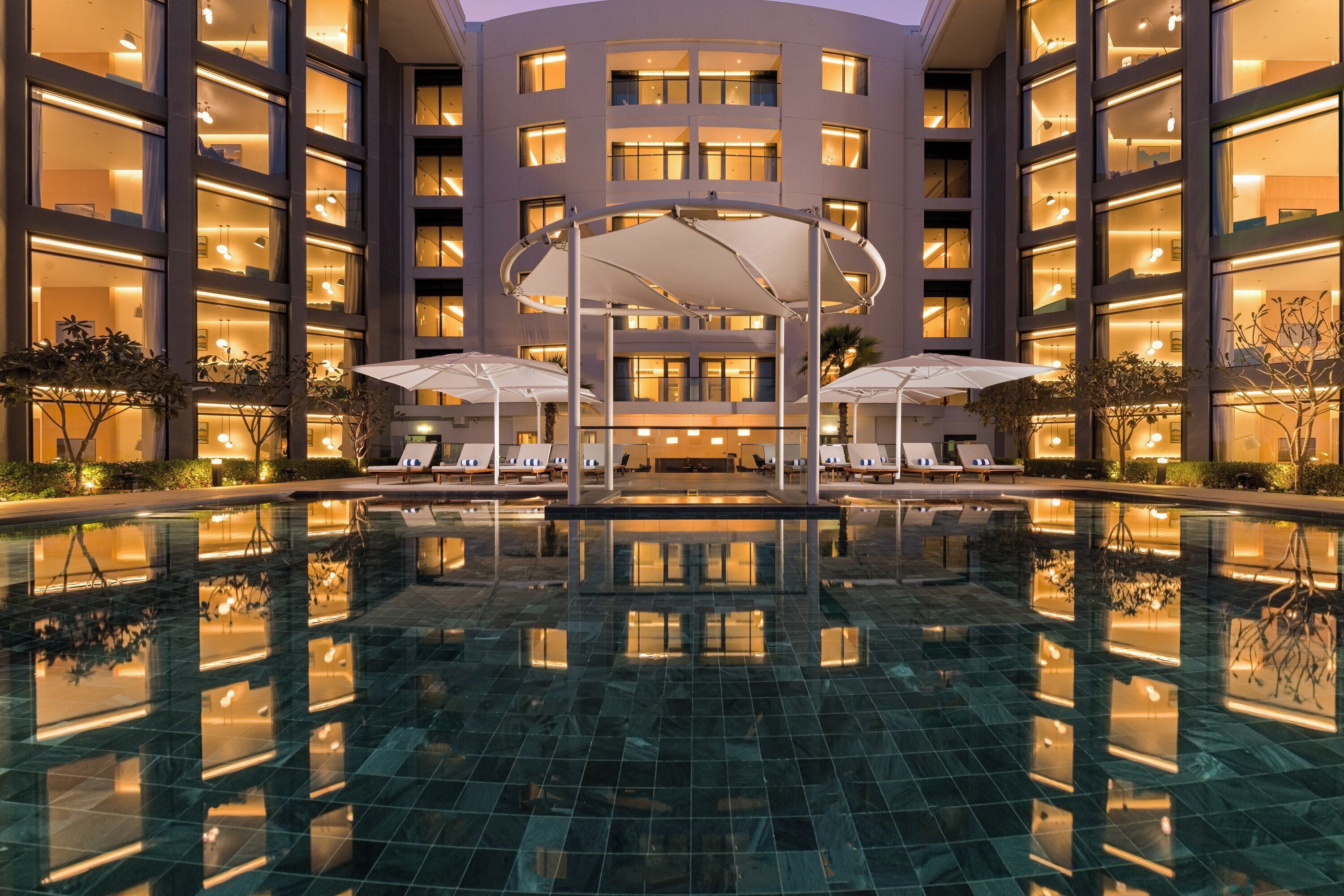 Un hotel con piscina central, varios pisos y zonas de estar al aire libre.