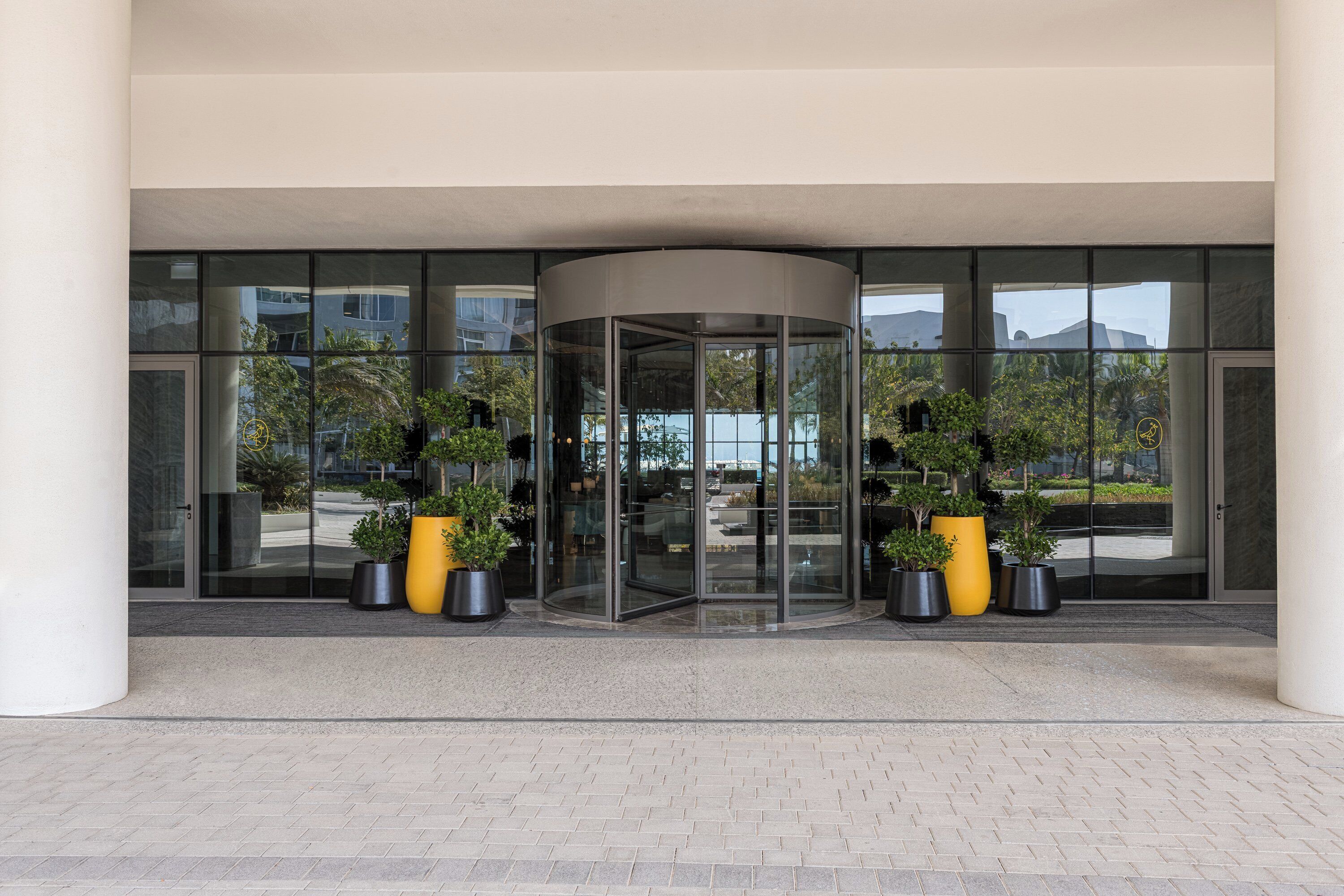 A revolving door entrance with glass panels, potted plants, and a paved area.