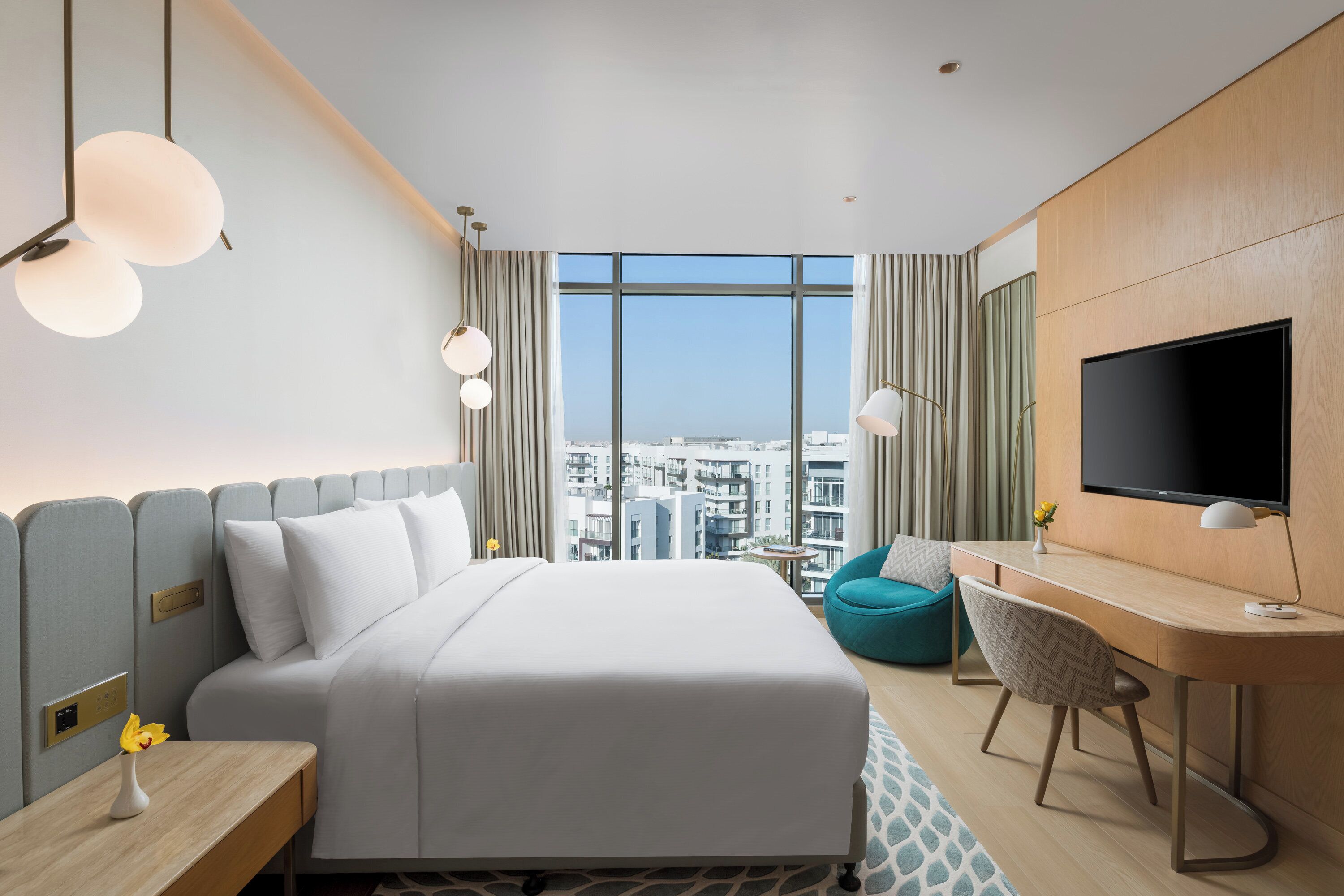 A hotel room with a bed, a desk, a TV, and a view of the city.