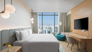 A hotel room with a bed, a desk, a TV, and a view of the city.
