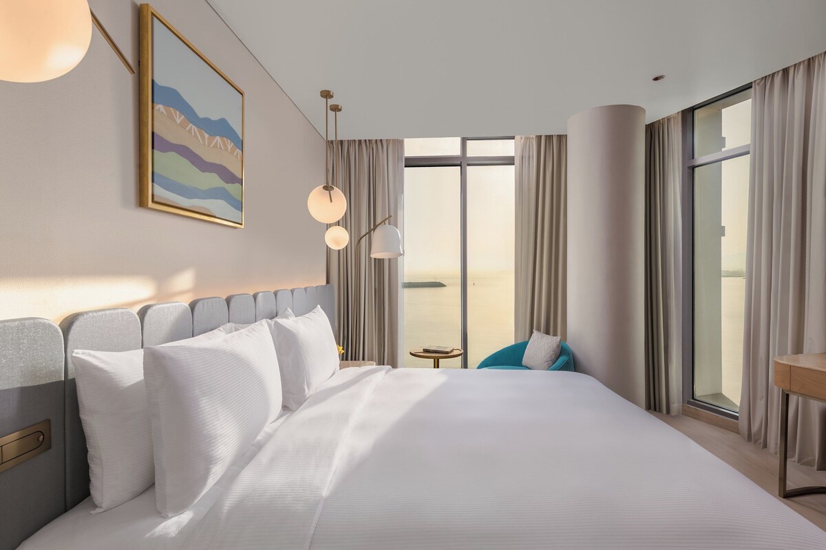 Ein Hotelzimmer mit einem großen Bett, Blick auf die Stadt, einem kleinen Tisch und einem Stuhl.