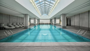 En stor indendørs swimmingpool med ovenlys, liggestole og et moderne design.