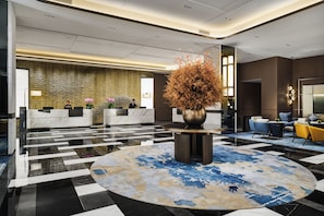 A modern lobby with a reception desk, seating area, and a decorative plant centerpiece.