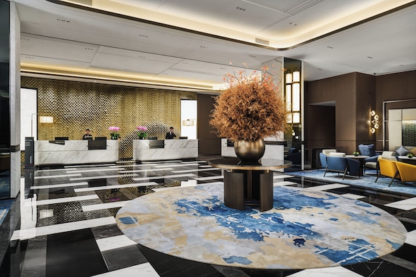 A modern lobby with a reception desk, seating area, and a decorative plant centerpiece.