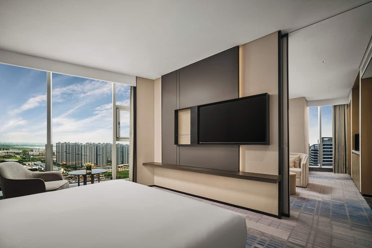 Ein modernes Hotelzimmer mit einem großen Bett, einem flachbildfernseher an der Wand und einem Balkon mit Blick auf die Stadt.