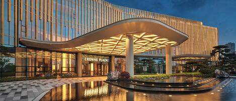 A modern building with a curved entrance and a reflective water feature in front.