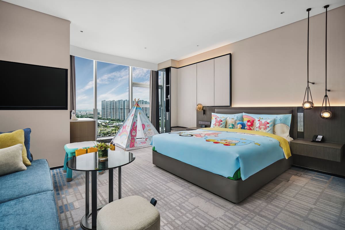 Ein modernes Hotelzimmer mit einem großen Bett, einer Couch, einem kleinen Tisch und Blick auf die Stadtlandschaft.