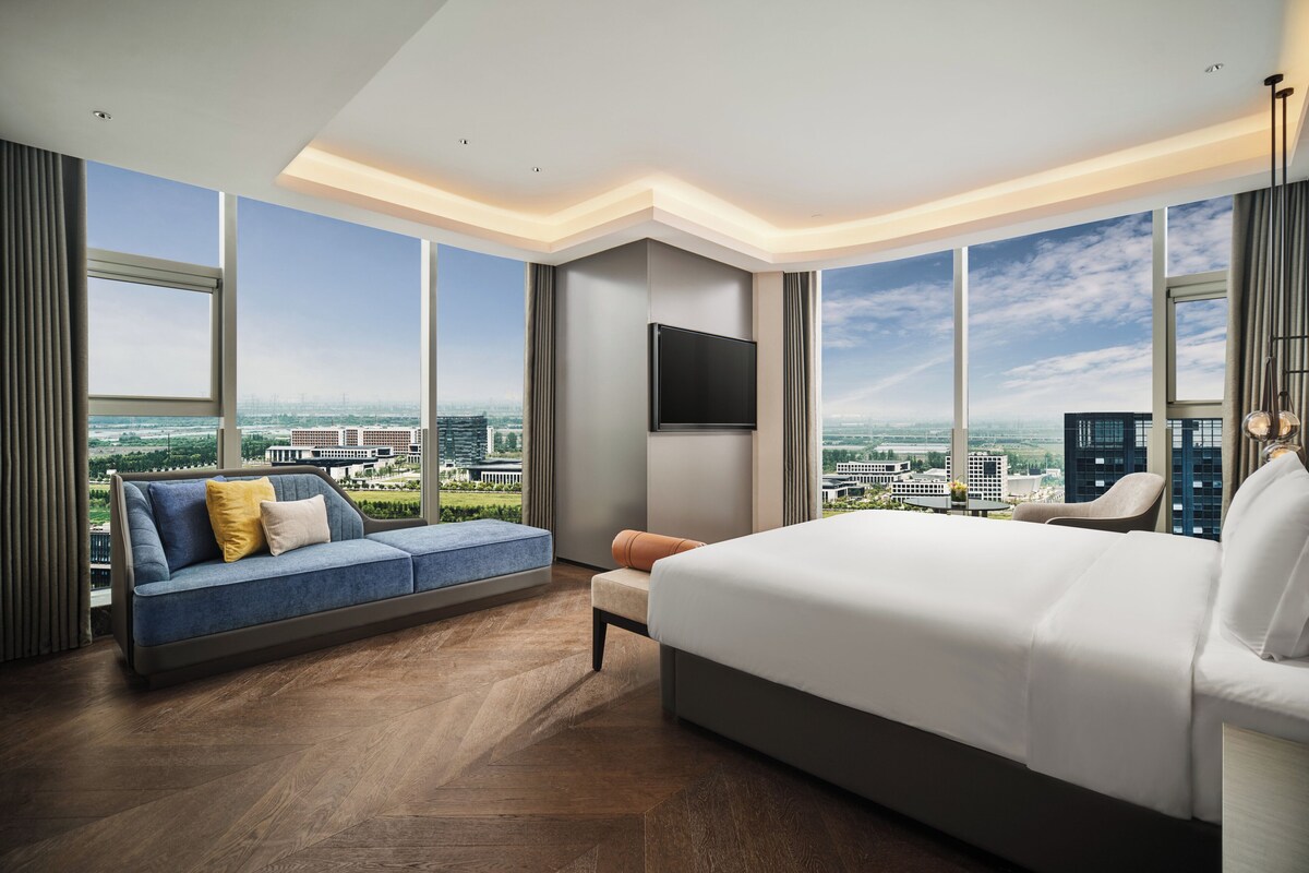 Une chambre d’hôtel moderne dotée d’un grand lit, d’un canapé, d’une télévision et offrant une vue sur la ville.