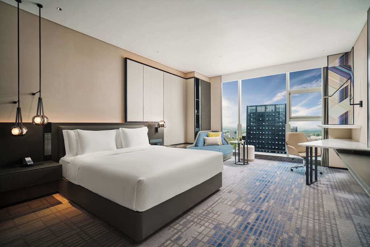 Ein modernes Hotelzimmer mit einem großen Bett, einem Schreibtisch, einem Sessel und Blick auf die Stadt.