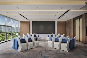 Une salle de conférence dotée d’un grand écran, de tables rondes et de chaises, ainsi que de grandes fenêtres offrant une vue sur la ville.
