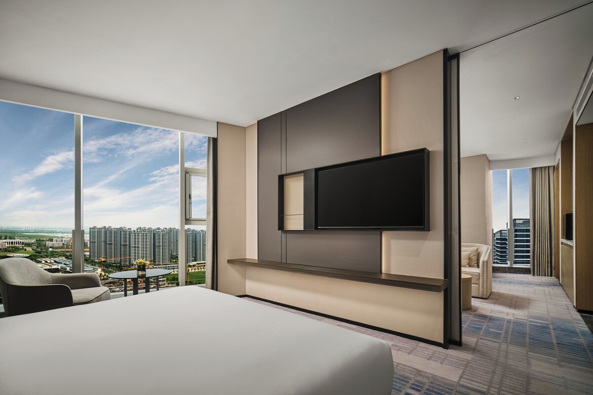 Une chambre d’hôtel moderne dotée d’un grand lit, d’un téléviseur à écran plat fixé au mur et d’un balcon offrant une vue sur la ville.