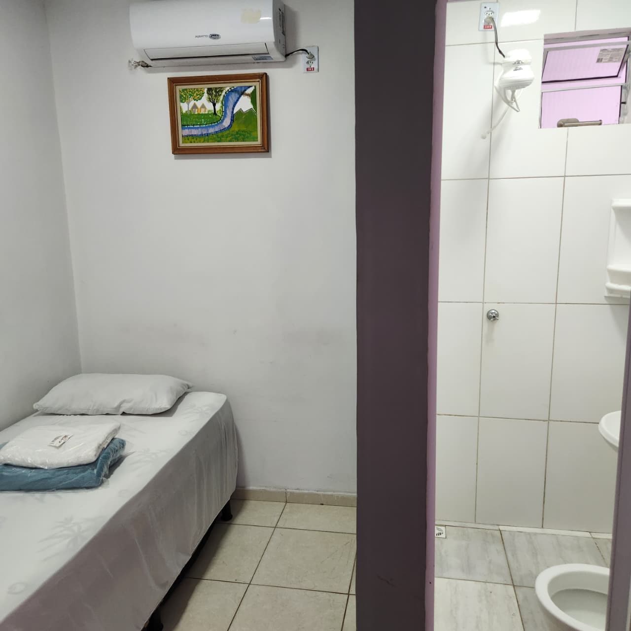 Une petite chambre avec un lit simple, des oreillers et un tableau accroché au mur.