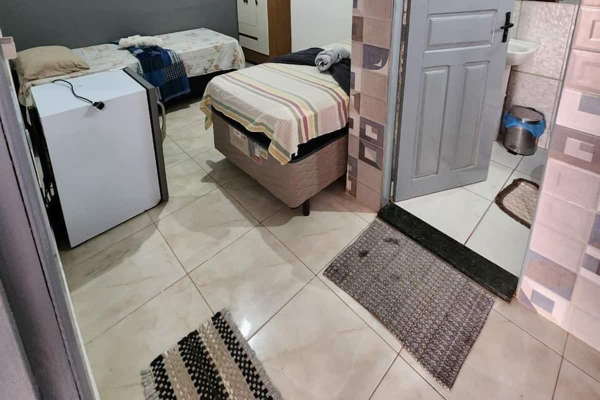 Une chambre à coucher de taille réduite, comprenant un lit, une armoire, une petite table et un réfrigérateur.