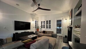 Un soggiorno moderno con televisione a schermo piatto, ventilatore a soffitto e zona pranzo con tavolo e sedie.