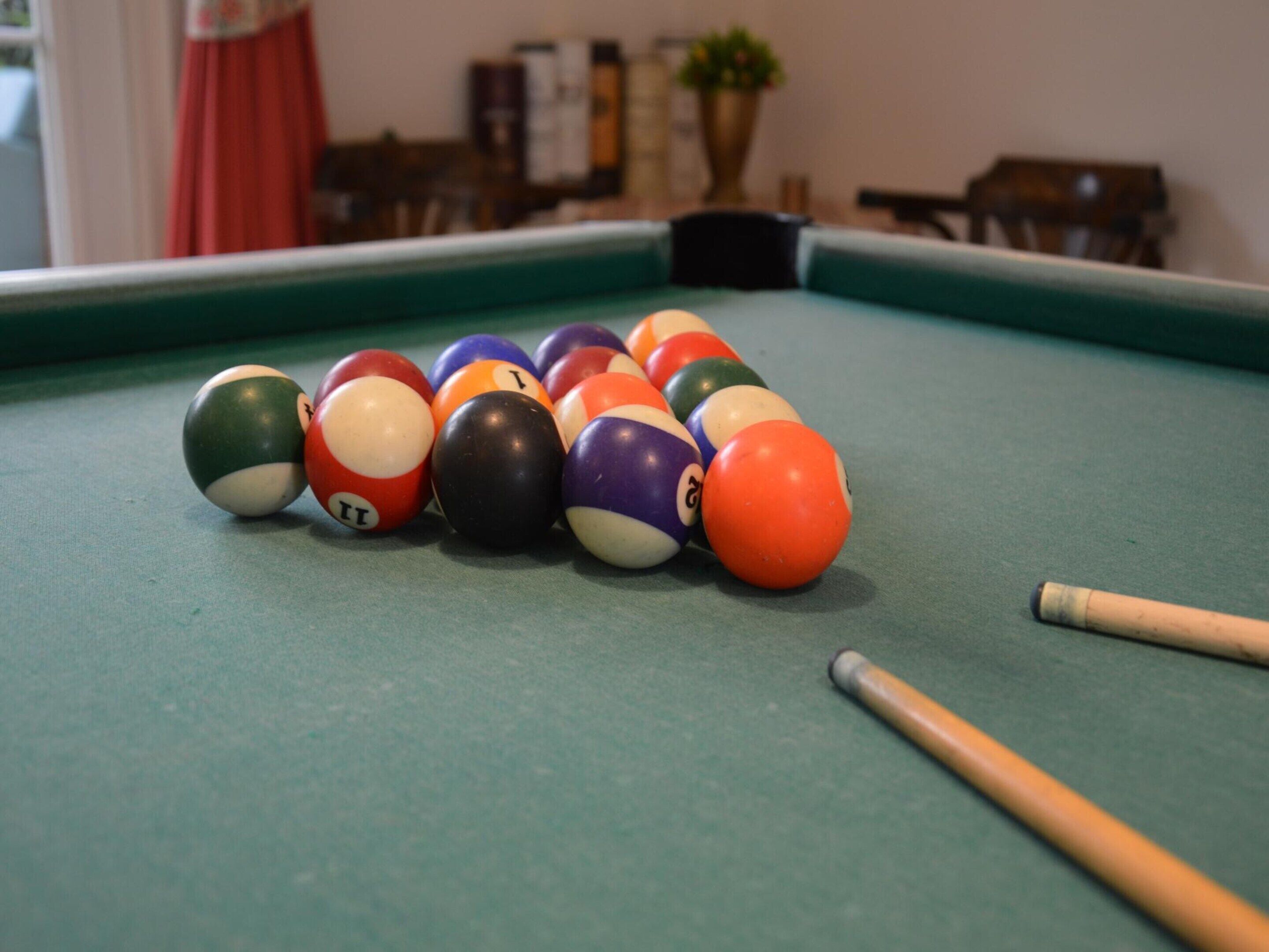 A pool table with a set of billiard balls and two pool cues.