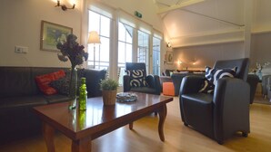 A spacious living room with a wooden coffee table, a black leather sofa, and a black armchair. There are large windows allowing natural light, and a painting is visible on the wall. - Holiday Home in Noordbeemster With Bubble Bath (Noordbeemster)