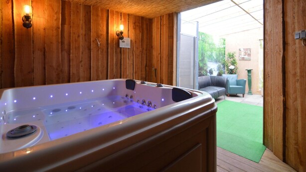 A wooden room with a hot tub, wooden walls, and a sliding glass door leading to an outdoor area. - Holiday Home in Noordbeemster With Bubble Bath (Noordbeemster)