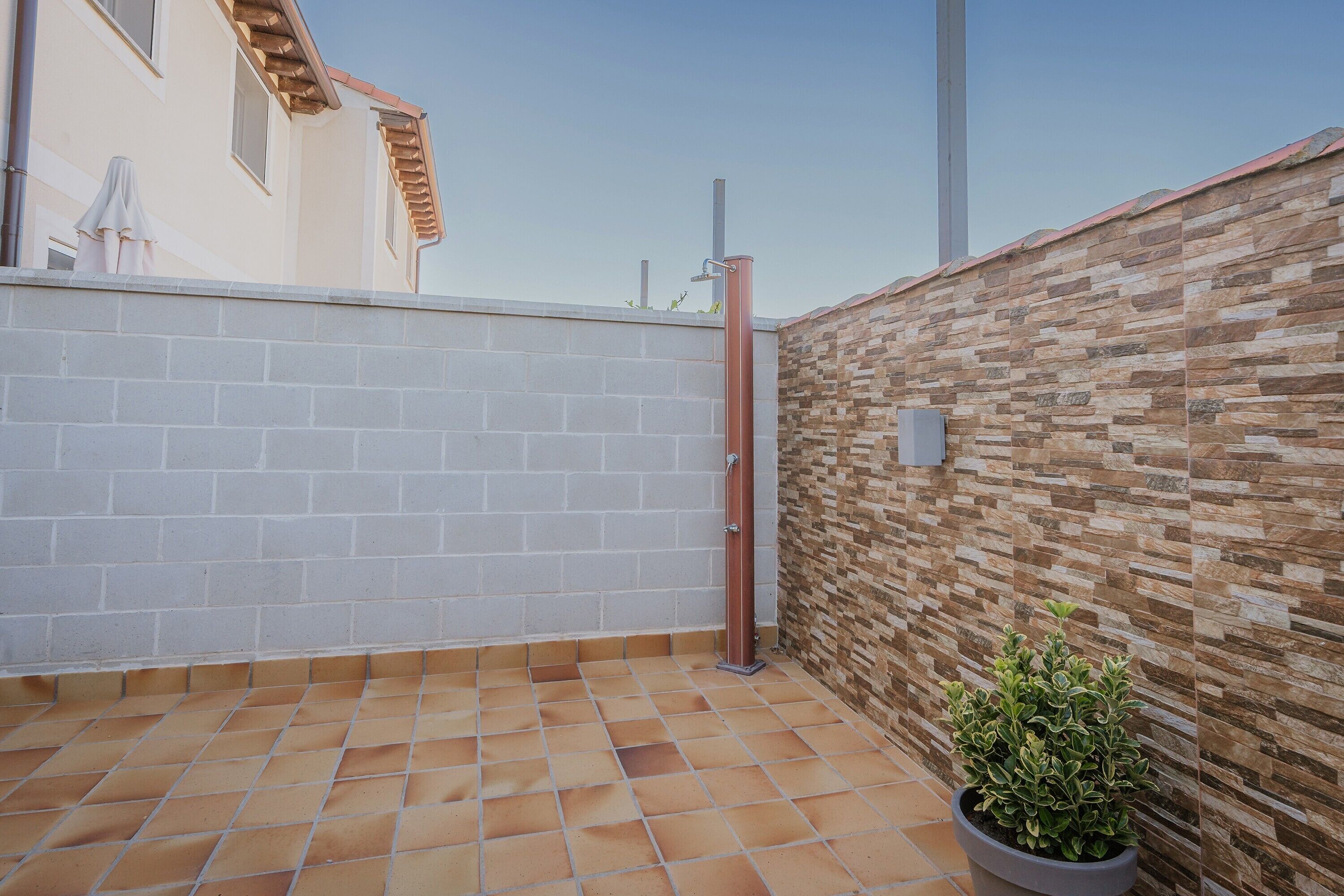 Un patio piastrellato con una pianta in vaso, un muro in mattoni e un cancello in metallo.