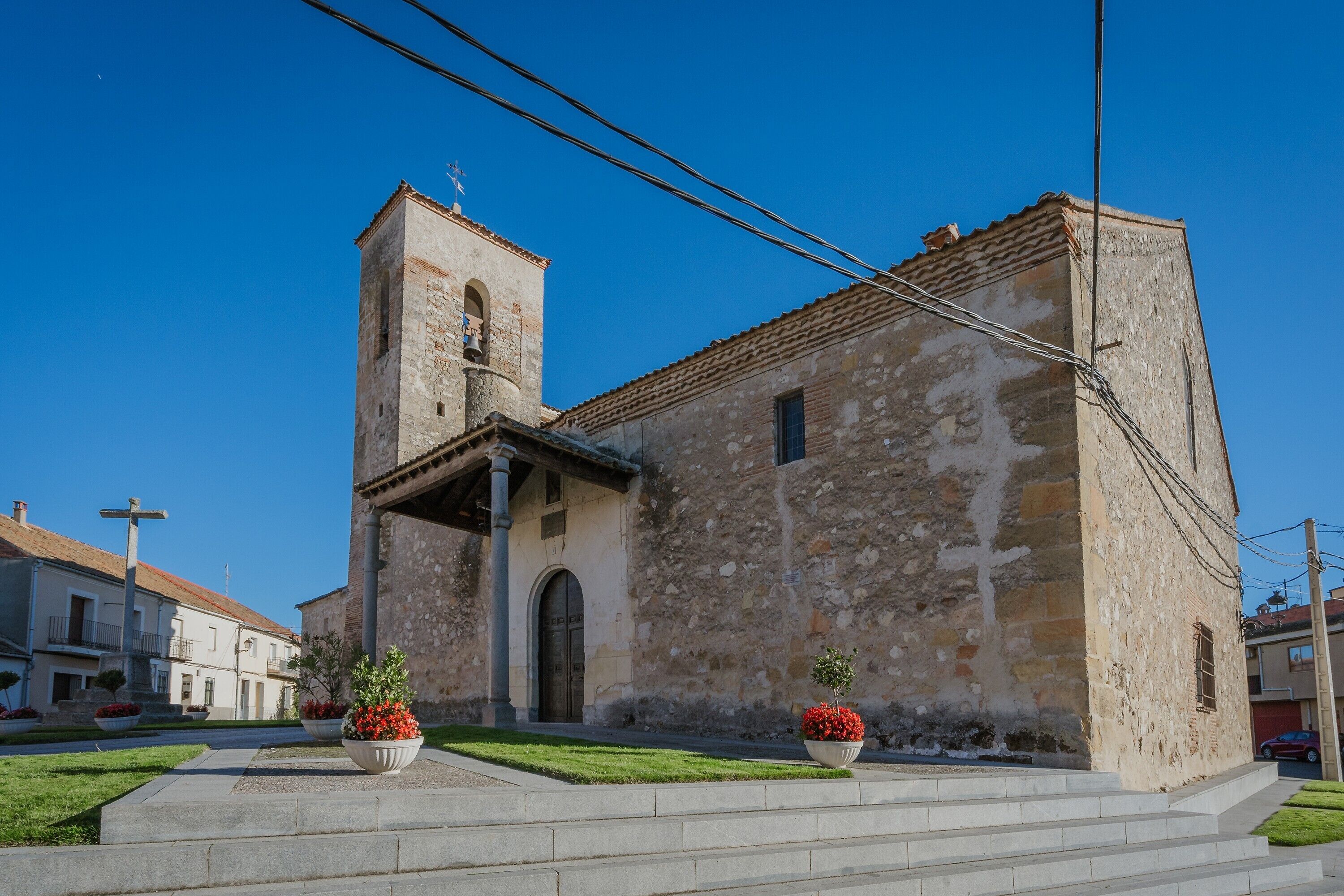 Un edificio histórico de piedra con un campanario, escalones que conducen a la entrada y plantas en macetas.