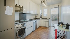 Une cuisine moderne équipée d’un lave-linge, d’un lave-vaisselle et d’un coin repas avec une table en verre et des chaises rouges.