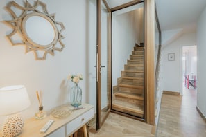 Un escalier menant à l’étage supérieur, un miroir fixé au mur, un bureau avec une lampe et un vase rempli de fleurs.
