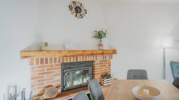 A dining area with a brick fireplace, a clock, and a vase with flowers.