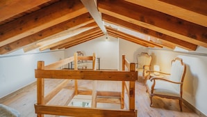 Une pièce mansardée en bois, avec un plafond en pente, des poutres apparentes et une petite table entourée de chaises.