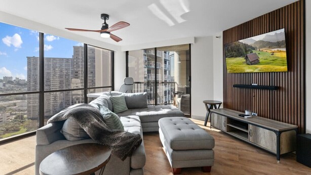 A modern living room with a large TV, a sofa, a coffee table, and a balcony with a city view. - Downtown Honolulu AC, W/D, Free Parking, Kitchen (Honolulu)