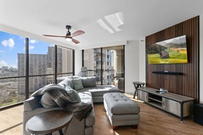 Un salon moderne doté d’un grand téléviseur, d’un canapé, d’une table basse et d’un balcon offrant une vue sur la ville.