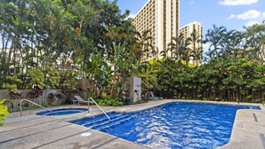A swimming pool with a small hot tub, surrounded by lush tropical plants and palm trees, with tall buildings in the background. - Downtown Honolulu AC, W/D, Free Parking, Kitchen (Honolulu)