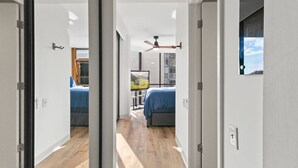 A modern hotel room with a wooden floor, two beds with blue bedding, a ceiling fan, and a large window with a cityscape view. - Downtown Honolulu AC, W/D, Free Parking, Kitchen (Honolulu)