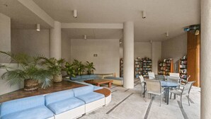 A spacious indoor area with a long blue sofa, a coffee table, and a dining table with chairs. There are several bookshelves filled with books and a few potted plants. - Downtown Honolulu AC, W/D, Free Parking, Kitchen (Honolulu)