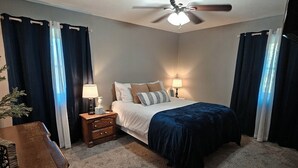 A bedroom with a bed, two bedside tables with lamps, a ceiling fan, and dark curtains. - “Relax, Unwind & Explore at Trailhead Hideaway – Mena’s Best Getaway!”

 (Mena)