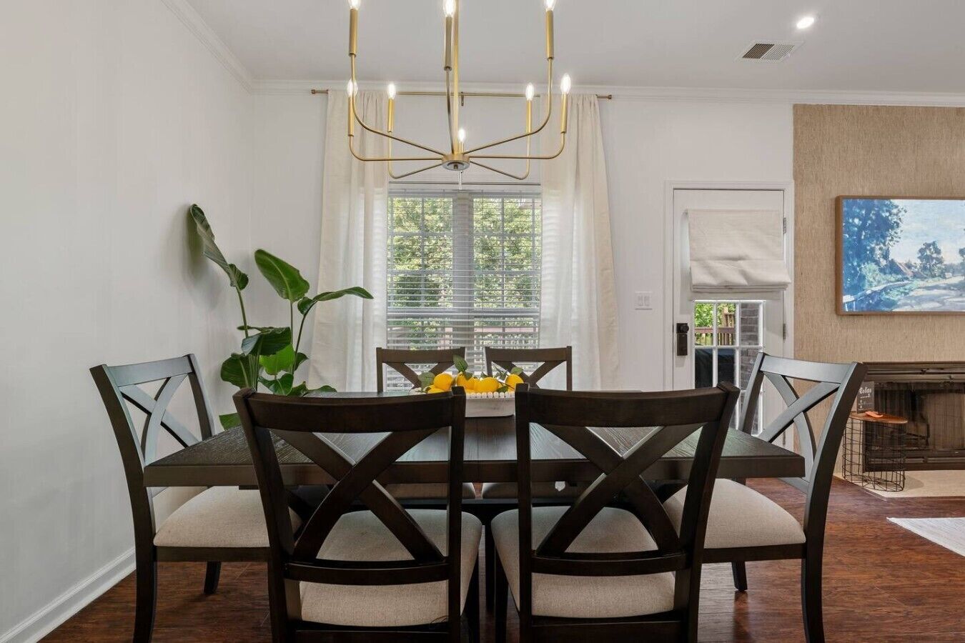 A dining area with a table and chairs, a chandelier, a plant, and a window with blinds.