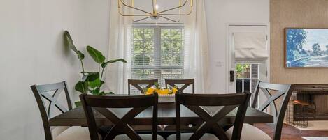 A dining area with a table and chairs, a chandelier, a plant, and a window with blinds.