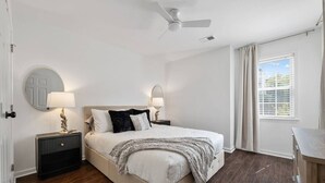A bedroom with a bed, two bedside tables with lamps, a ceiling fan, a window with curtains, and a radiator. - Beautiful 3 Bedroom On The River! (Vestavia Hills)