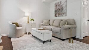 A living room with a sofa, armchair, ottoman, side table, lamp, and a painting on the wall. - Beautiful 3 Bedroom On The River! (Vestavia Hills)