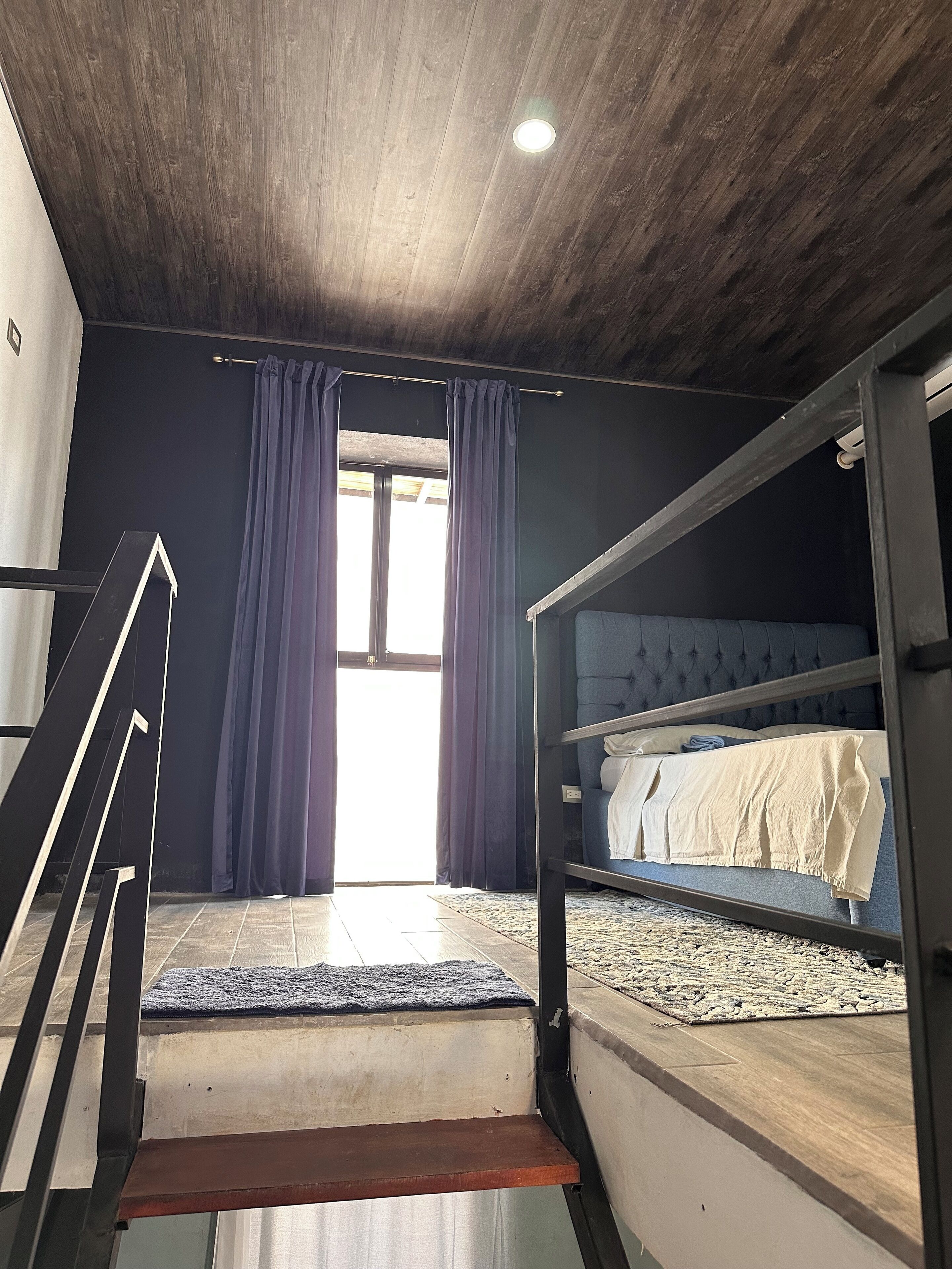 A room with a bunk bed, a staircase, and a window with curtains.