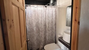 Un baño pequeño con puerta de madera, cortina de ducha, inodoro y lavabo.