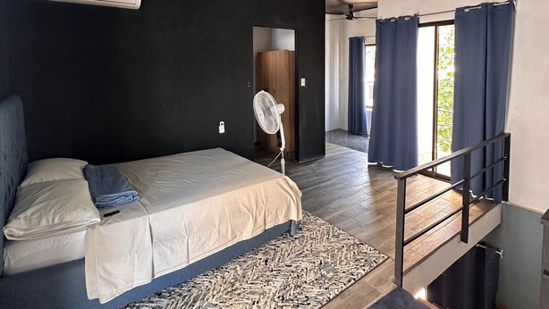 Un dormitorio con cama, ventilador, alfombra estampada y una escalera.