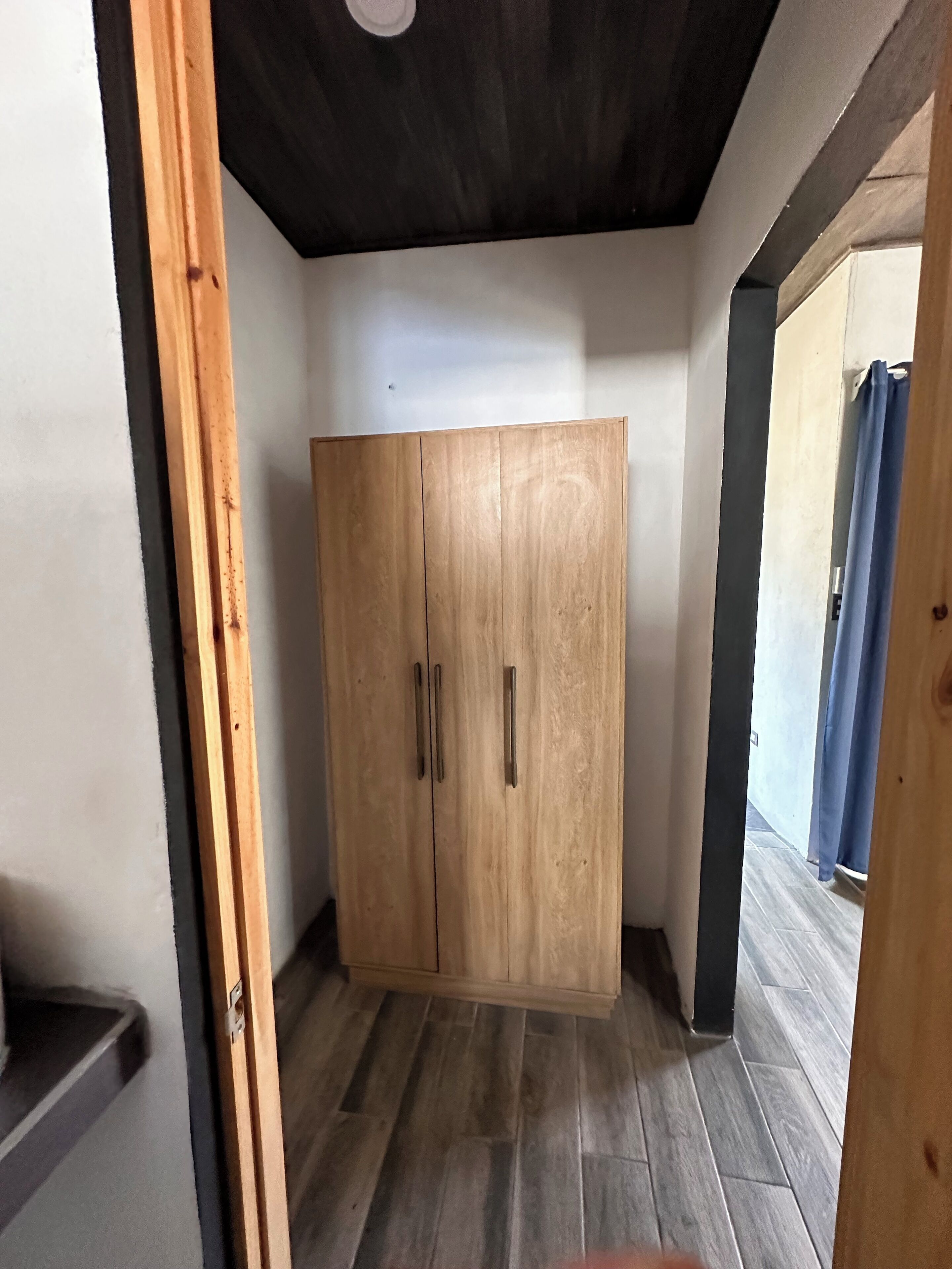 A room with a wooden wardrobe, a tiled floor, and a ceiling with exposed beams.